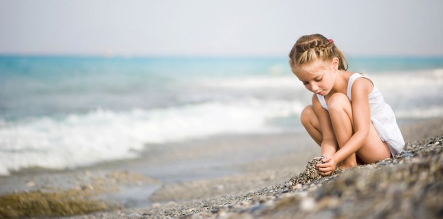 photo of girl playing with pebbles on the beach