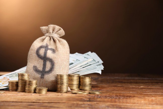 Money Bag, dollar banknotes and stacked coins on wooden table